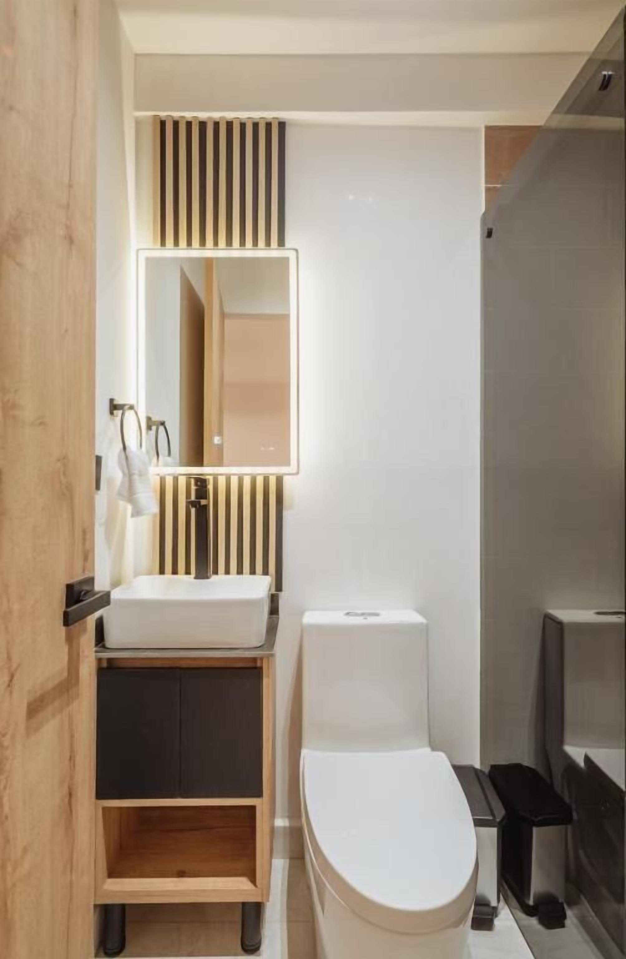 Une salle de bain moderne avec un lavabo blanc, des toilettes et un miroir à rayures verticales.
