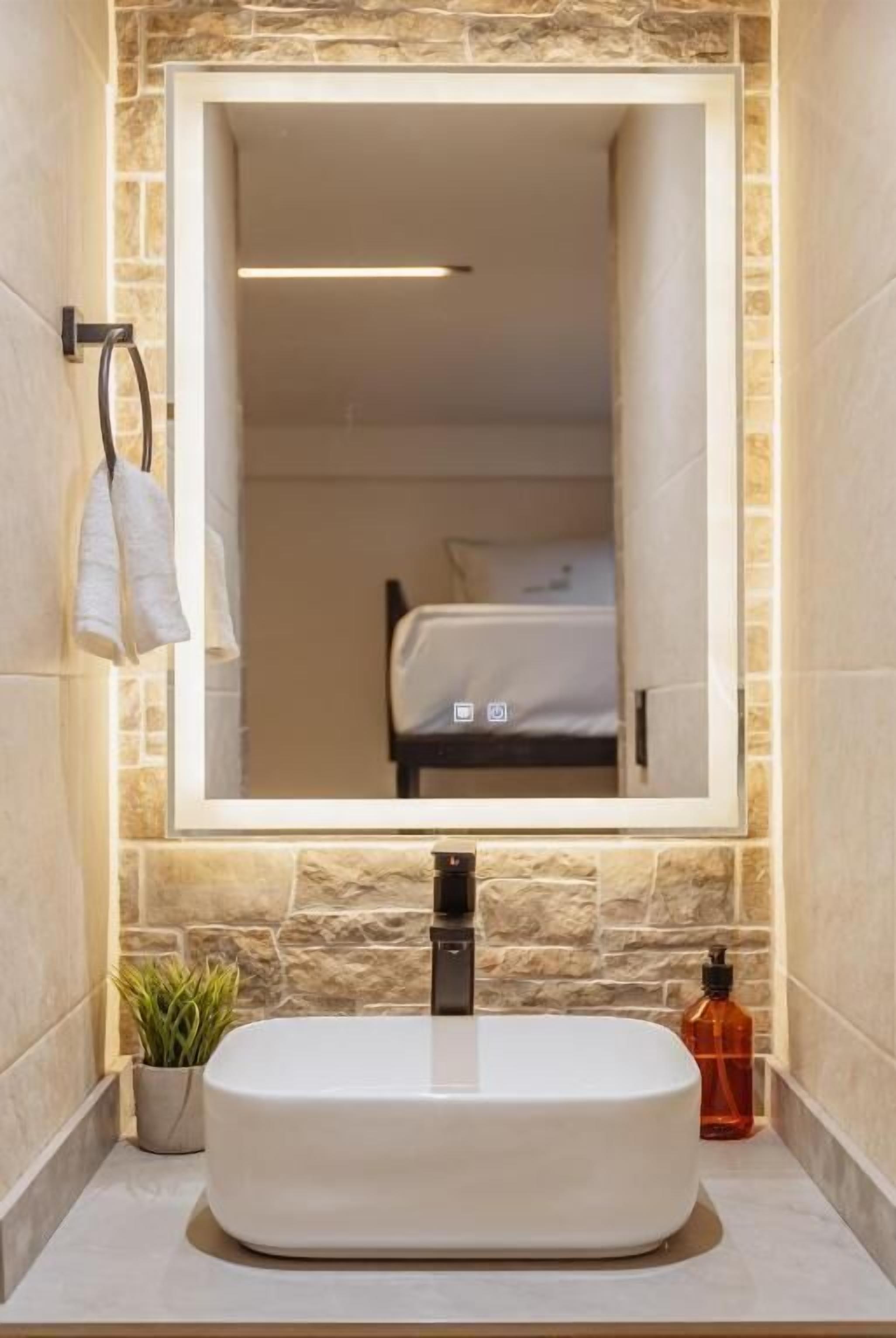 Une salle de bain avec un grand miroir, un lavabo blanc, un porte-serviettes, une plante en pot et un flacon de savon.