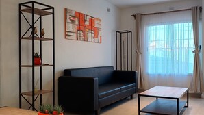 Een moderne woonkamer met een zwarte bank, een houten salontafel en een metalen plank met decoratieve objecten.