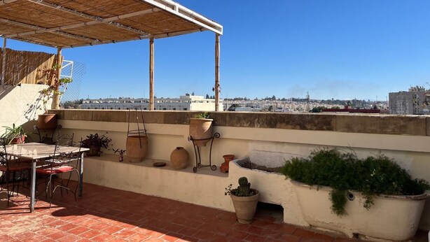 A rooftop terrace with a table and chairs, potted plants, and a view of the cityscape. - Rooftop del quinto (Fès)