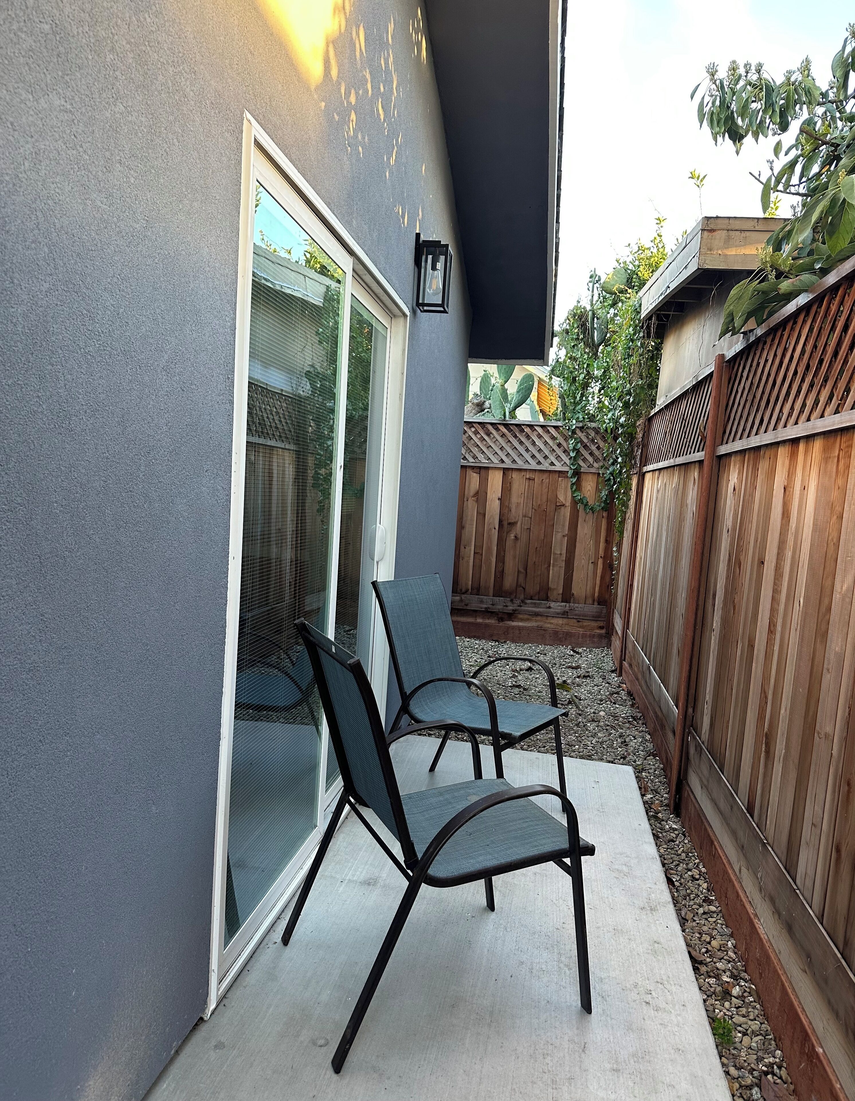 Une terrasse avec deux chaises et une table, une clôture en bois et une maison à l’extérieur grise.