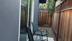 En uteplats med två stolar och ett bord, ett trästaket och ett hus med en grå fasad.