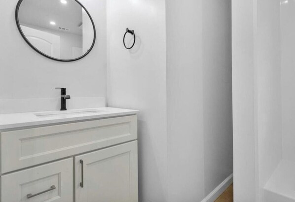A modern bathroom with a white vanity, a round mirror, and a towel ring on the wall. - Serene 2-bedroom house in Oakland perfect for your getaway (Oakland)