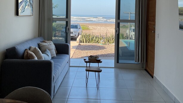 Ein modernes Wohnzimmer mit einem großen Schiebeglasfenster, das auf einen Balkon mit Blick auf einen Strand führt.