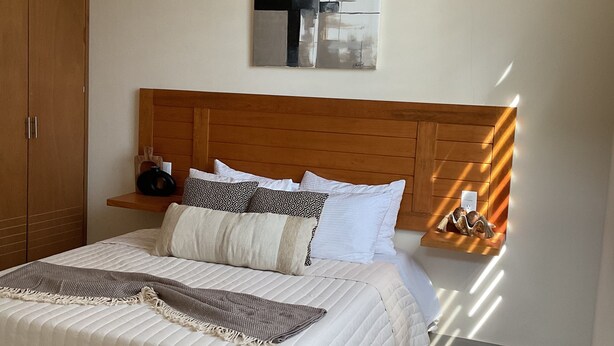 Ein Schlafzimmer mit einem großen Bett, einem Holzkopfstück und einem an der Wand befestigten abstrakten Gemälde.