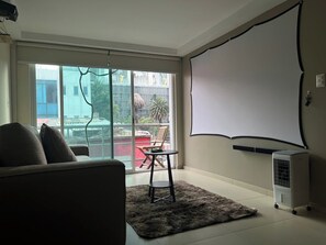 Une pièce dotée d’une grande fenêtre, d’un écran de projection, d’un canapé, d’une petite table et d’un tapis.