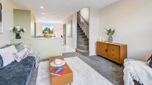 Een moderne woonkamer met een bank, een salontafel en een kast. Er is een trap die naar een andere kamer leidt.