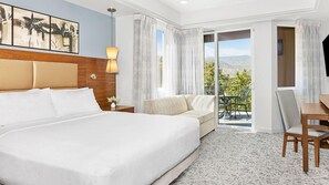 Ein Hotelzimmer mit einem großen Bett, einer Sitzecke, einem Esstisch und einem Balkon mit Bergblick.