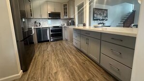 A modern kitchen with stainless steel appliances, grey cabinets, and a wooden floor. - Monterey Bay Escape (Seaside)