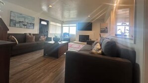 A spacious living room with a fireplace, dark sofas, and a large TV. - Monterey Bay Escape (Seaside)