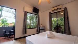 A hotel room with a bed, a desk, a chair, a ceiling fan, and a window with curtains. - Hotel Manuel antonio beracha (Quepos)