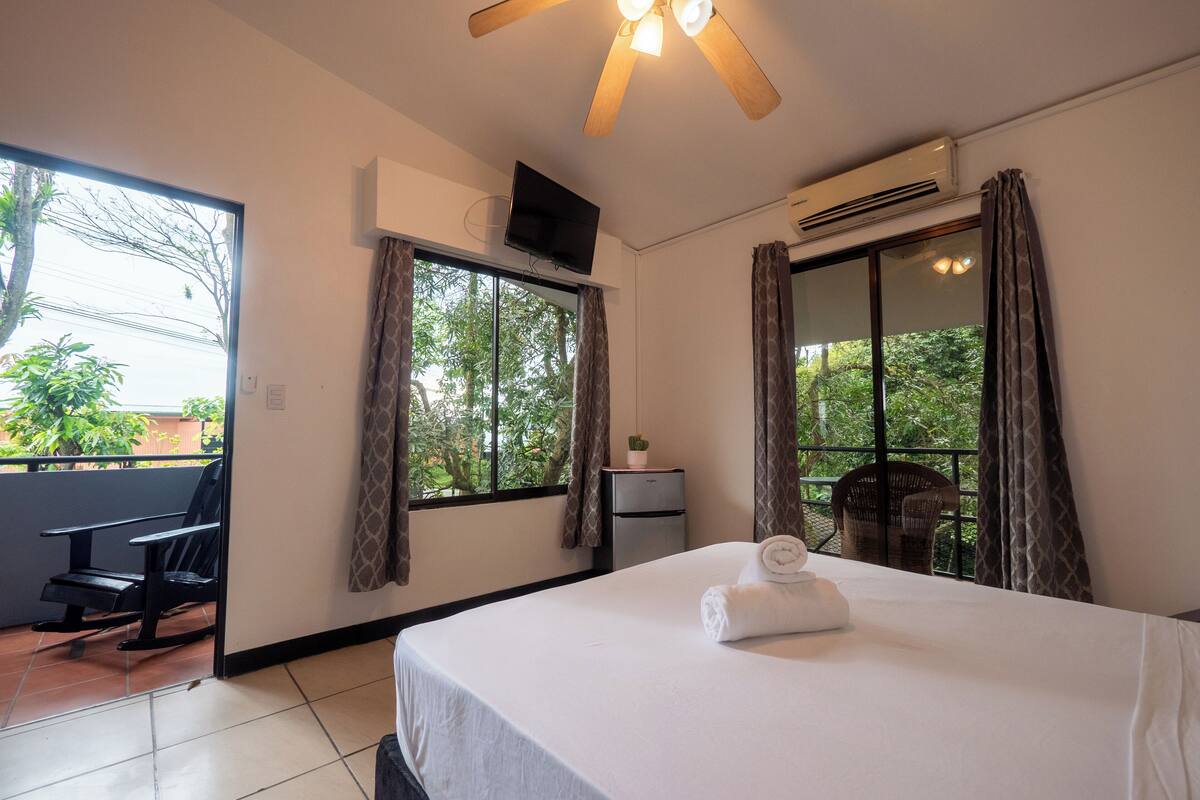 A hotel room with a bed, a desk, a chair, a ceiling fan, and a window with curtains.