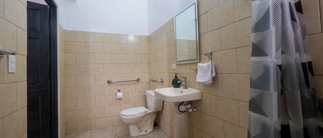 A bathroom with beige tiles, a white toilet, a sink, a mirror, and a shower curtain.