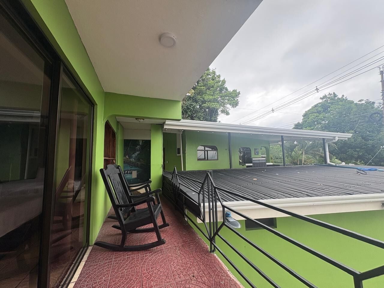 Un balcon doté d’une rambarde en métal, une paire de fauteuils à bascule et une vue sur la verdure environnante.