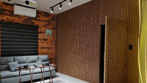 Un salon moderne avec un canapé gris, deux tables en bois, un mur au motif de briques et une cloison en bois.