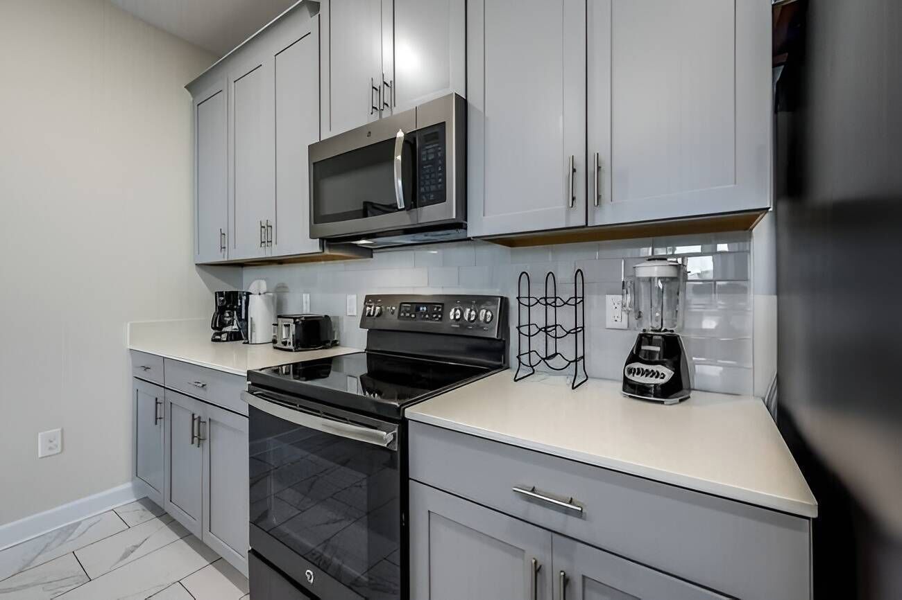 A modern kitchen with grey cabinets, a microwave, a stove, a coffee maker, and a blender.