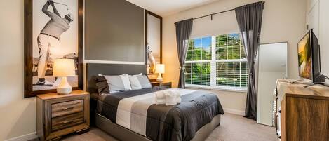 Une chambre à coucher avec un lit, des tables de chevet, une télévision et une fenêtre avec des rideaux.