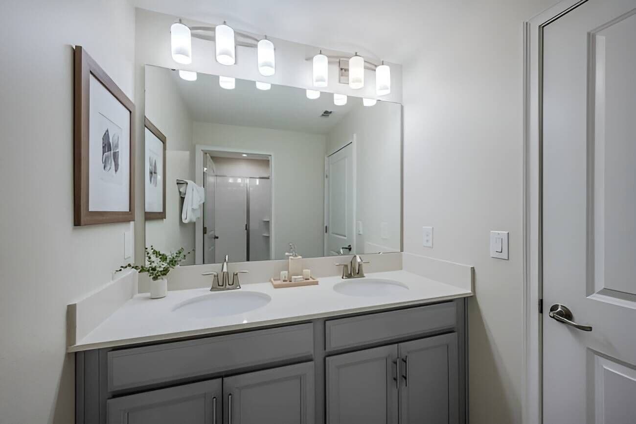 Une salle de bain moderne avec deux lavabos, un grand miroir et un luminaire placé au-dessus du miroir.