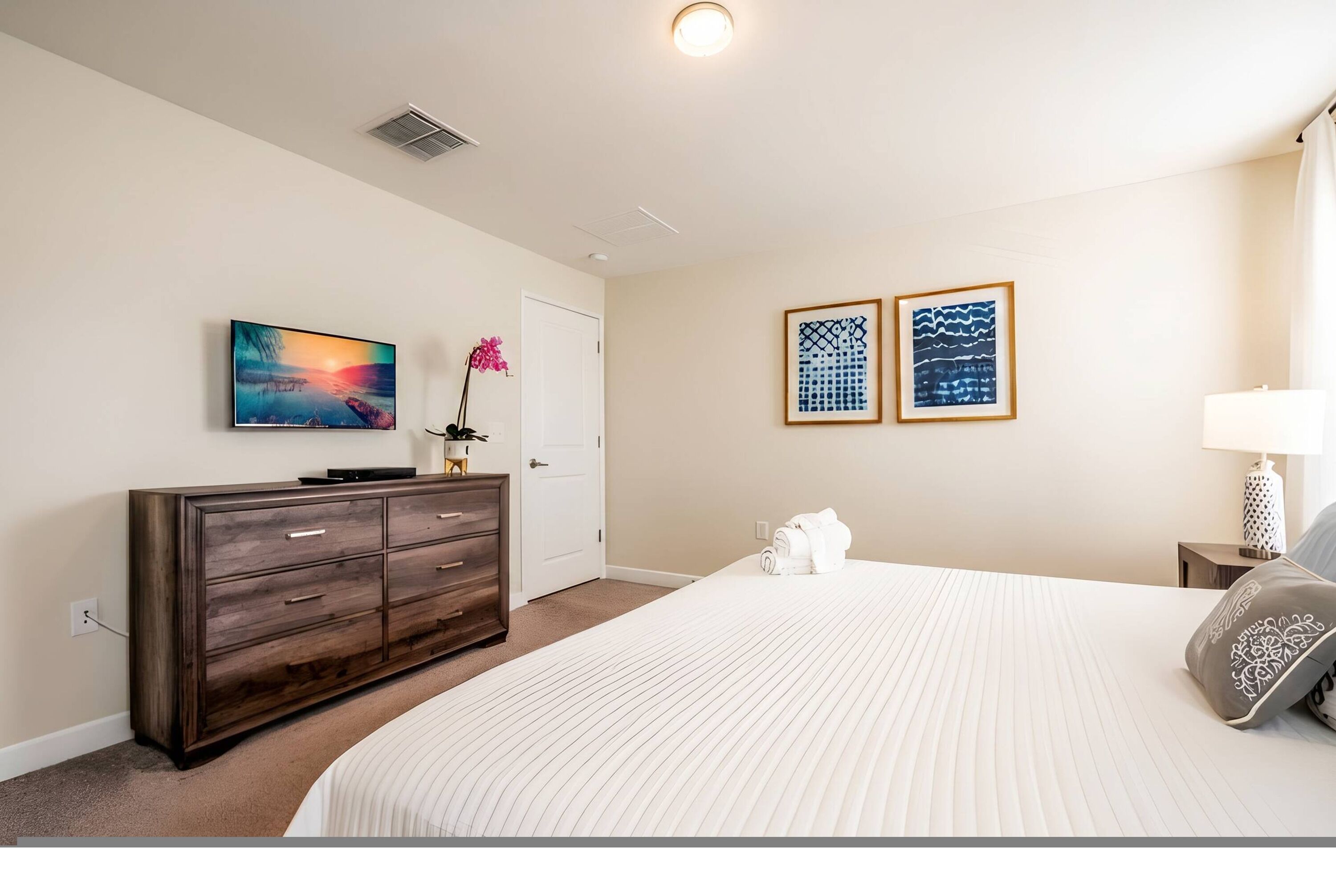 A bedroom with a bed, dresser, two framed pictures, and a lamp.
