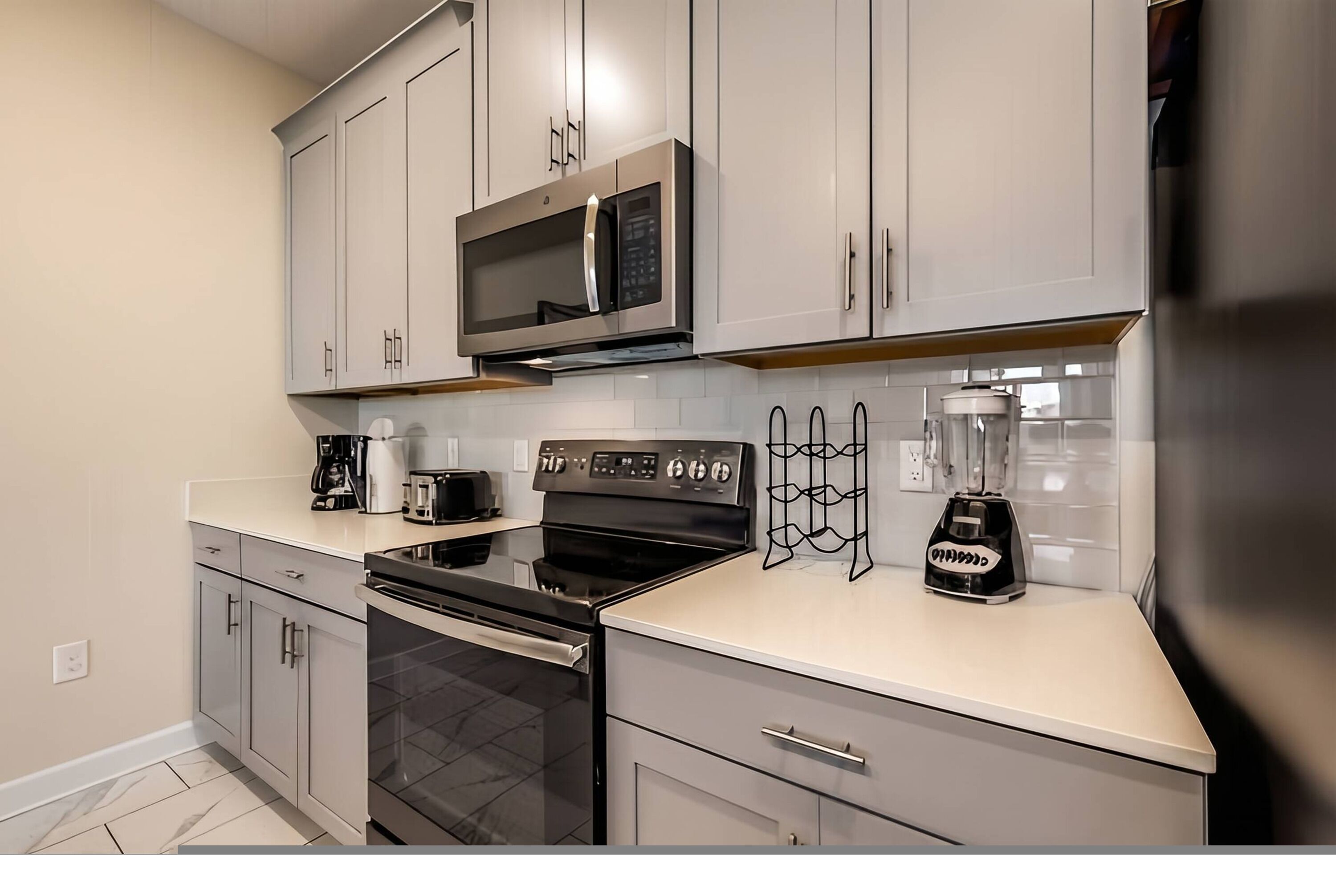 A modern kitchen with grey cabinets, a built-in microwave, a stove, a coffee maker, and a blender.