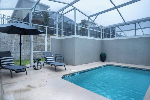 A pool area with lounge chairs and an umbrella, enclosed by a glass structure. - 4BR Luxury Home at Champions Gate With Pool (Davenport)