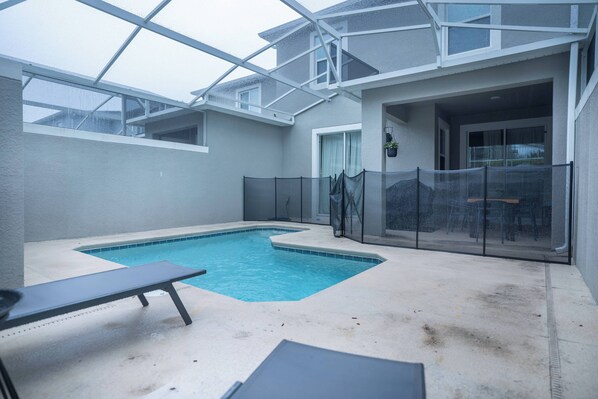 A swimming pool with a glass enclosure, a lounge chair, and a patio area. - 4BR Luxury Home at Champions Gate With Pool (Davenport)