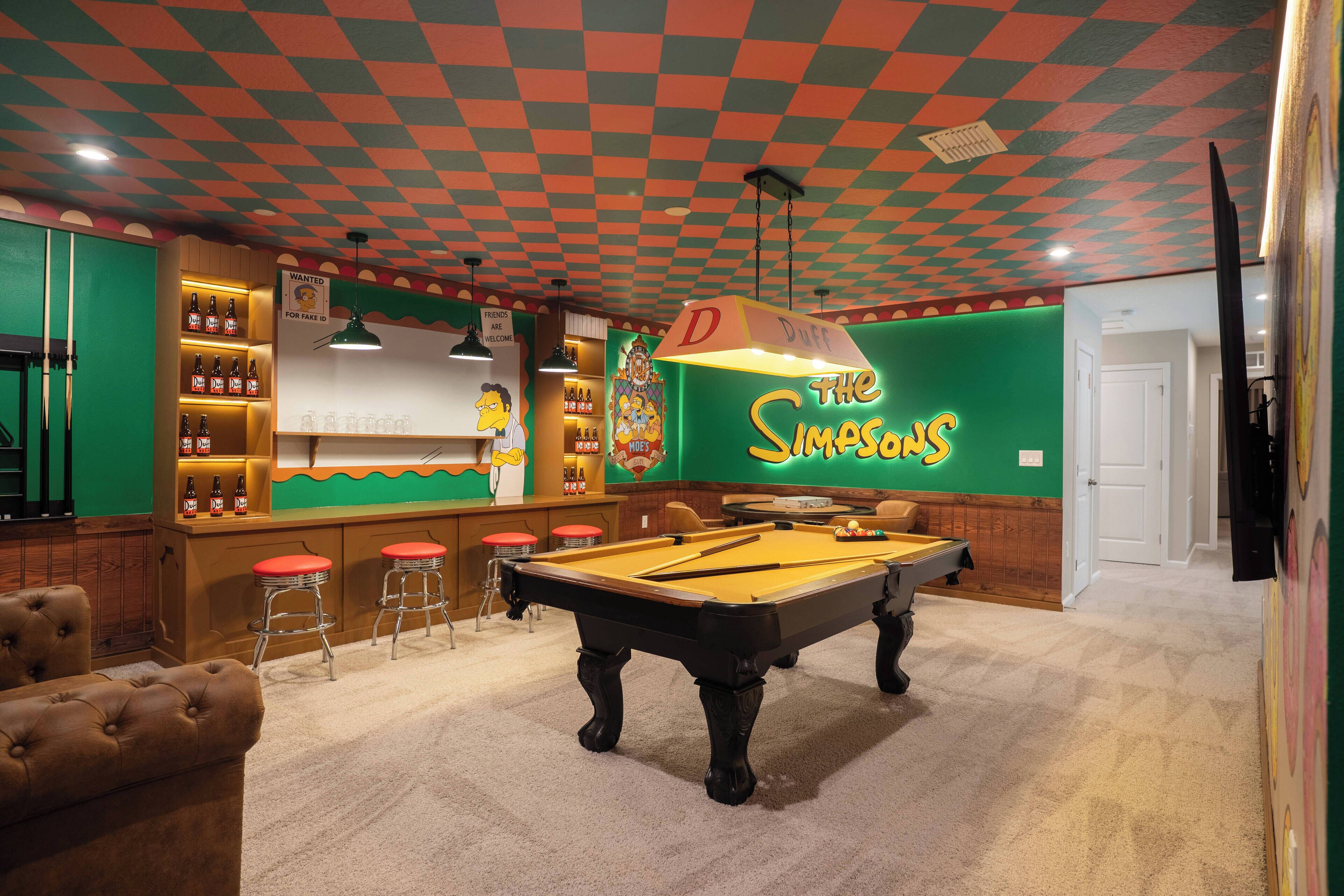 A pool table in a room with a Simpsons-themed wall and a bar area with stools.