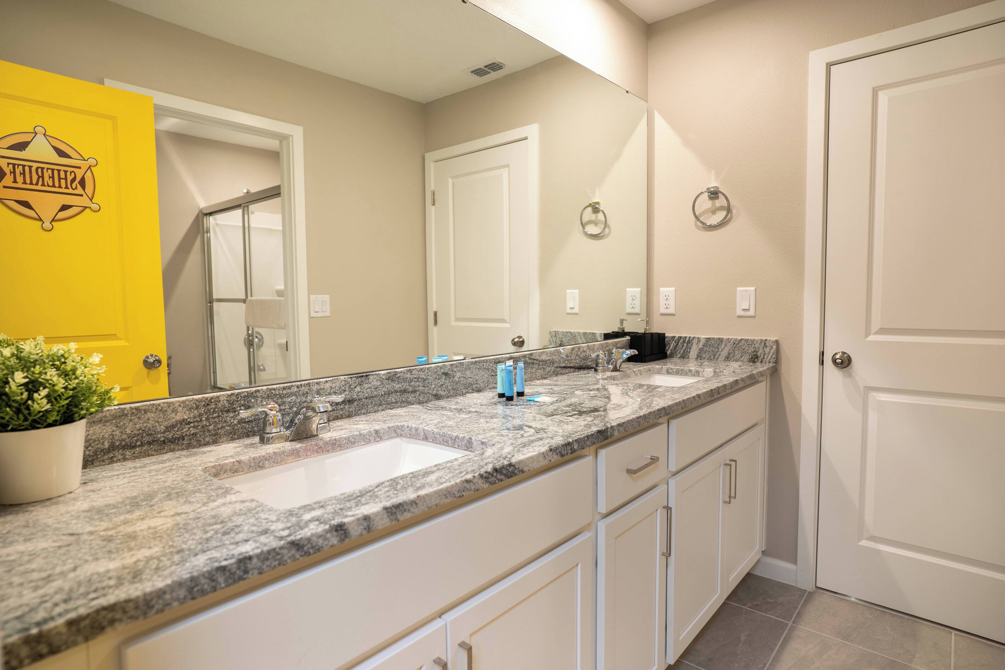 A bathroom with a granite countertop, white cabinets, a yellow door, and a large mirror.