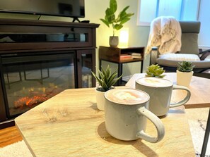 A cozy living room with a fireplace, two mugs on a wooden table, and a comfortable couch. - Walk to Grouse Gondola · Ski/Hike/Bike Base · 3BR Family Retreat (North Vancouver)