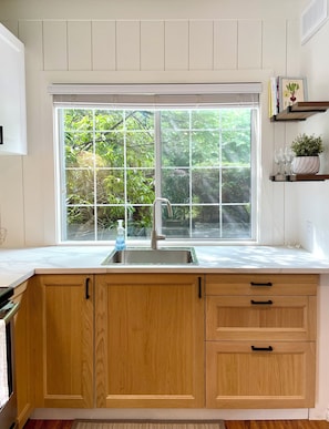 A kitchen with wooden cabinets, a stainless steel sink, and a window with a view of greenery. - Walk to Grouse Gondola · Ski/Hike/Bike Base · 3BR Family Retreat (North Vancouver)