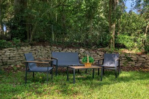 An outdoor seating area with three chairs and a table, surrounded by a stone wall and lush greenery.