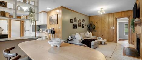 A modern kitchen with white cabinets, a dining table with chairs, and a living area with a sofa and coffee table.