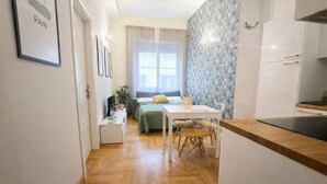 Ett kompakt bostadsutrymme med ett litet kök, en matplats och ett sovrum med ett fönster.