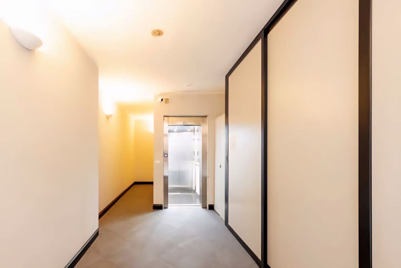 Un couloir étroit doté d’un plancher de couleur claire, de murs blancs et d’une porte au fond qui donne sur une autre pièce.