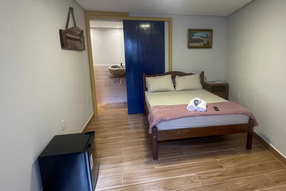 A bedroom with a bed, bedside table, and a small trash bin.