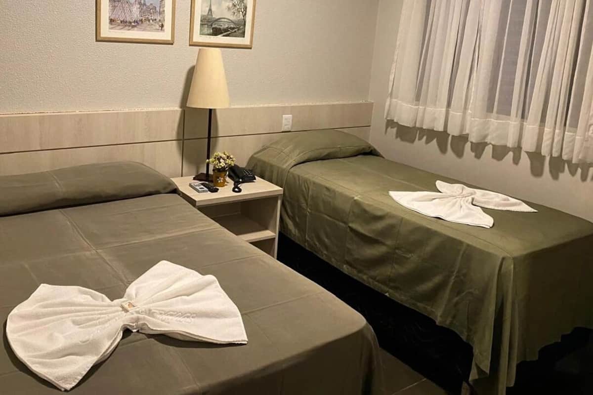 A hotel room with two beds, a nightstand with a lamp, and a telephone.