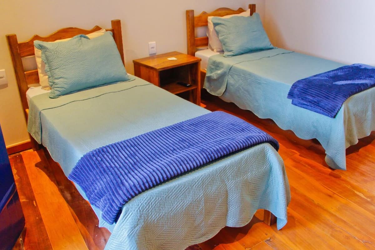 Two single beds with wooden headboards, a nightstand between them, and a wooden floor.
