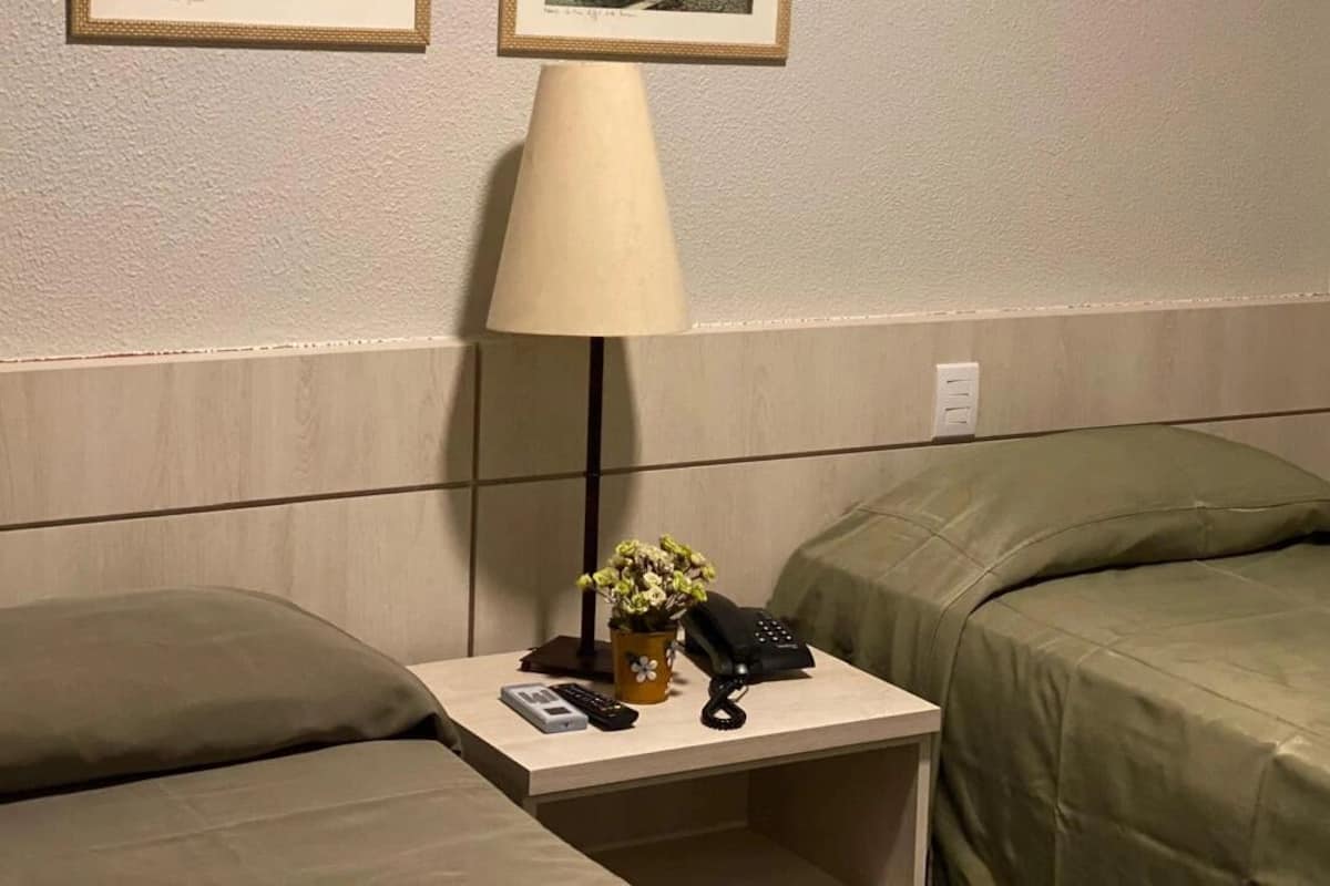 Una habitación de hotel con una cama, una mesita de noche con lámpara, un jarrón con flores y un teléfono.