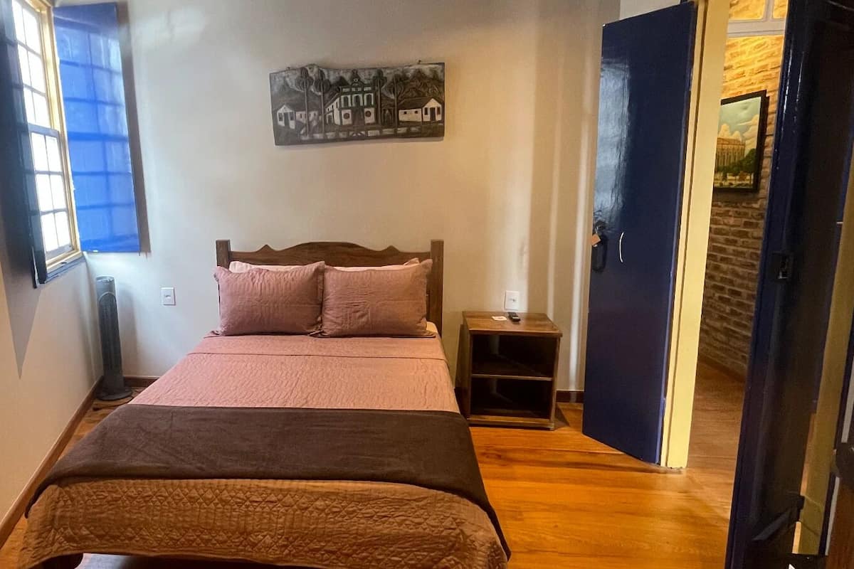 A bedroom with a bed, a nightstand, a wall-mounted artwork, and a door leading to another room.