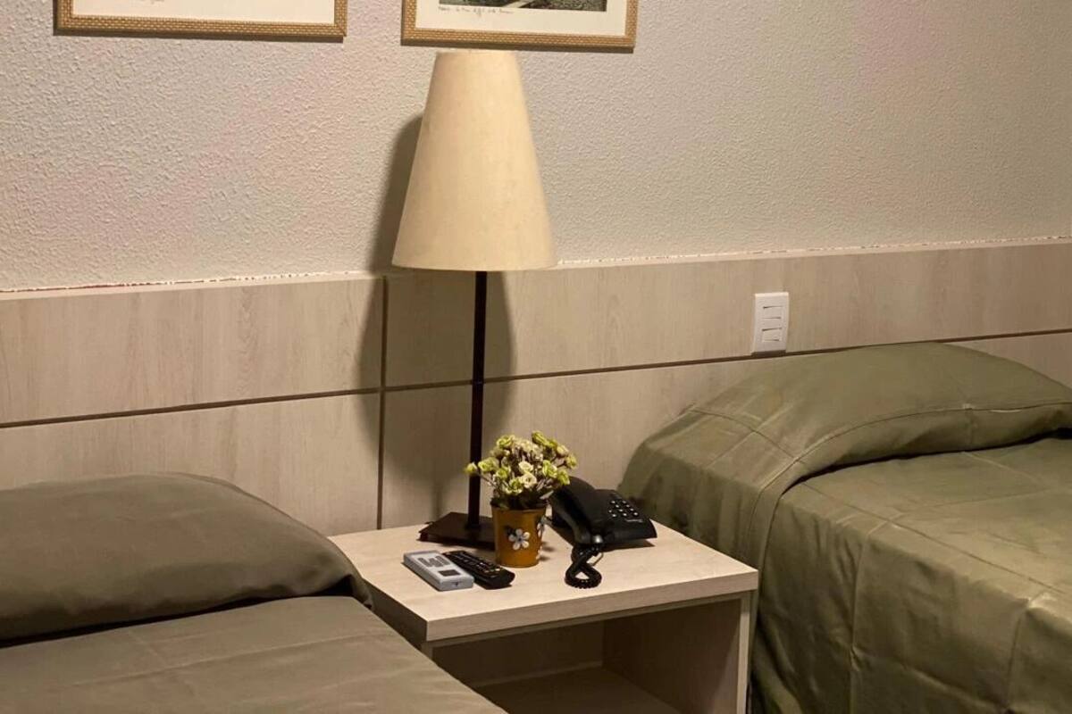 A hotel room with a bed, a bedside table with a lamp, a vase with flowers, and a telephone.