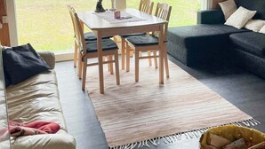 Ein gemütlicher Wohnbereich mit einem Holzesstisch, vier Stühlen, einer Couch und einem großen Fenster mit Seeblick.