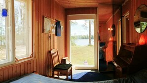 Ein Zimmer in einer Holzhütte mit einem Bett, einem Sessel, einem kleinen Tisch und einer Tür, die nach draußen führt.