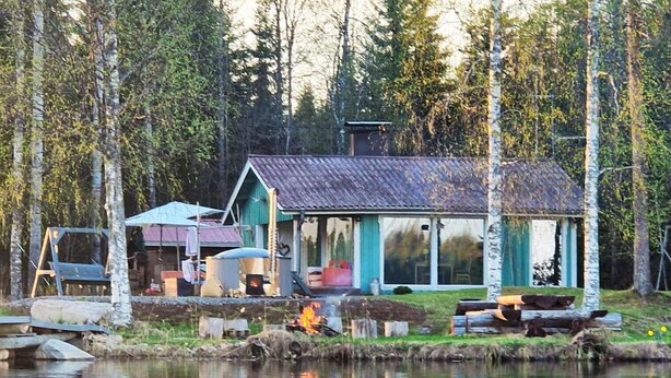 Eine Holzhütte am See mit Metalldach, einer Veranda und einer Feuerstelle.