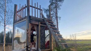 Eine Holzhütte mit Glastür, einer Holzleiter und einem Steinfundament.