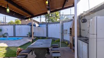 Um pátio coberto ao ar livre com piscina, churrasqueira e geladeira.