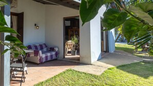 A covered outdoor seating area with a checkered sofa, a potted plant, and a tiled floor. - HOSTEL QUINTAL GUEST - Guarujá (Guarujá)