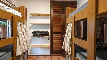 A dormitory room with bunk beds, a shelf with bags, and a wardrobe with sliding doors.