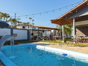 Un patio trasero con piscina, mobiliario exterior y zona de barbacoa.
