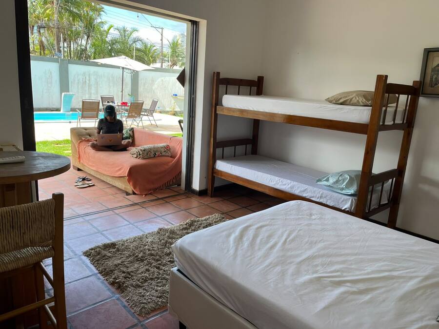 A room with a bunk bed, a sofa, a laptop on the sofa, and a view of a swimming pool outside.