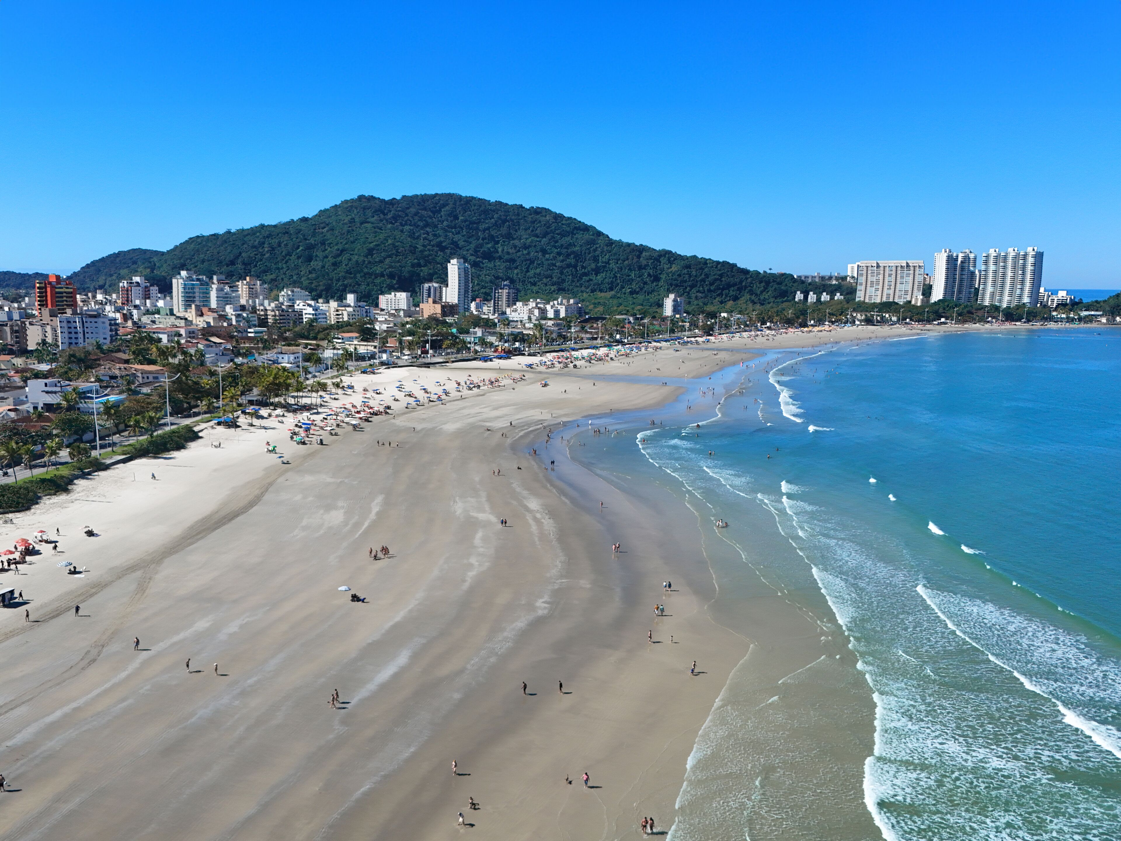 Una playa con una montaña al fondo, un paisaje urbano con edificios y un cielo despejado.